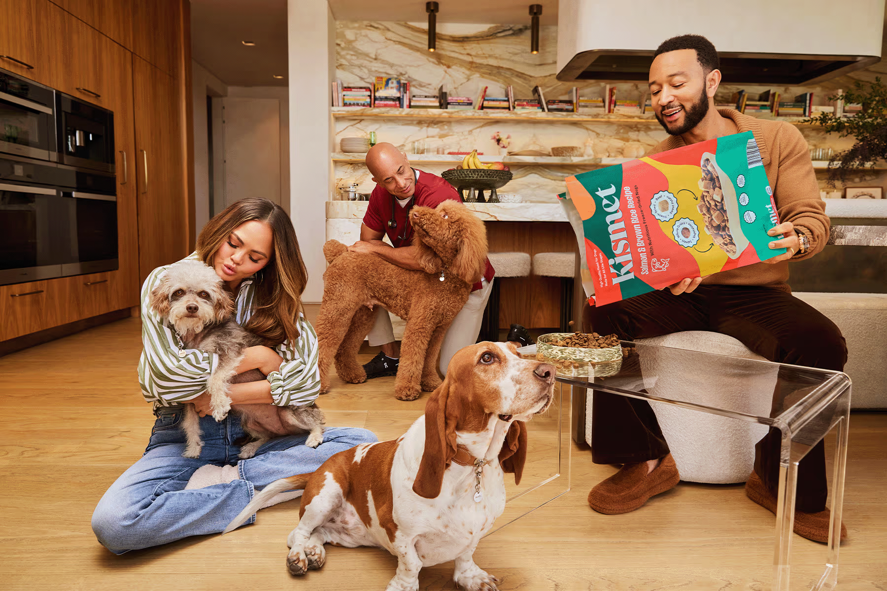 Chrissy, John and Dr. Kwane with dogs in a kitchen setting, with a bag of Kismet food for dogs.